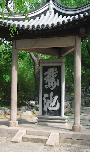 Small pavilion just large enough to contain a vertical stone sign with Chinese calligraphy in white with a black background reading 'goose pond'.